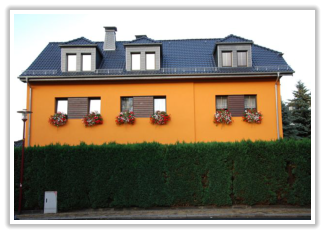 Gelbes Wohnhaus mit dunklem Schieferdach, Dachgauben und Blumenkästen